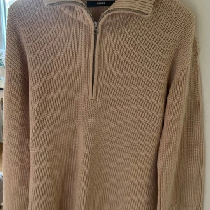 Beige stickad half zip-tröja BikBok - Säljer en beige stickad tröja från BikBok med half zip och hög krage. Tröjan har lång ärm och är ribbstickad för en snygg och avslappnad look. Perfekt för lager-på-lager och chill dagar.