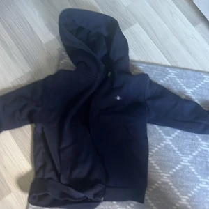 Mörkblå hoodie från GANT med dragkedja - Säljer en mörkblå hoodie från GANT i storlek L. Tröjan har huva, dragkedja framtill och är långärmad. Klassisk och stilren design med liten GANT-logga på bröstet. Perfekt för dig som gillar en enkel och snygg look.