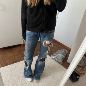 Lågmidjade, slitna jeans - Säljer mina gamla favorit jeans. Så snygga lågmidjade med slitningar och najs fickor bak. Jag är ca 170-172 och de är långa på mig. Knappen har gått av så istället är det ett snöre/rosett i midjan. 