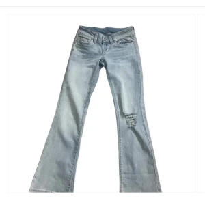 Ljusblå bootcut jeans med slitning - Snygga ljusblå jeans med bootcut-modell och slitning på ena benet. Klassisk femficksdesign och låg midja. Perfekta för en avslappnad och trendig look.