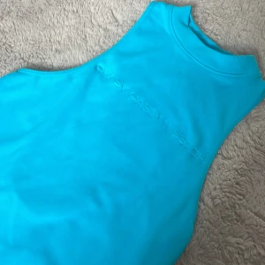 Turkos bodysuit från Carin Wester - Säljer en turkos bodysuit från Carin Wester med hög hals och ärmlös design. Toppen har ett stilrent, tight passform och diskret logga broderad framtill med öppen rygg