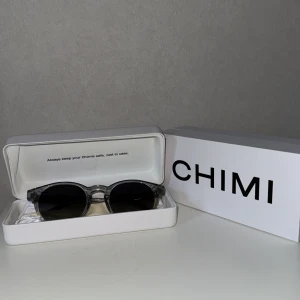 CHIMI 03 solglasögon - Snygga runda solglasögon från CHIMI med transparent grå båge och mörka linser. Sidorna har en glittrig silverdetalj som ger extra edge. Kommer med originaletui och box. Perfekta för dig som vill sticka ut med stilren design. Säljs då jag köpt ett par nya!                                          Modell - Chimi 03 - Grey 