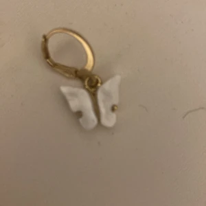 Guldiga örhängen med vita fjärilar - Superfina örhängen i guldton med hängande vita fjärilar. Fjärilarna har en snygg 3D-effekt och sitter fast i små guldfärgade ringar. Perfekta för dig som vill ha en söt och trendig detalj till din look.