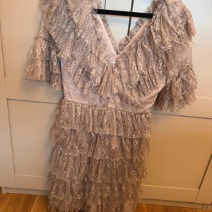 Beige spetsklänning med volanger - Romantisk beige kortklänning med flera lager volanger och spetsdetaljer. Djup v-ringning och korta ärmar med volang. Perfekt för dig som vill sticka ut med en feminin och bohemisk look.