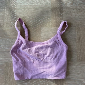 Ljusrosa ribbad linnetopp - Söt ljusrosa ribbad linnetopp med smala axelband och croppad passform. Perfekt för varma dagar eller som lager under en skjorta. Mjuk och stretchig känsla som gör den superbekväm.