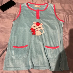 Blå ärmlös pyjamas med kattmotiv - Söt ljusblå ärmlös pyjamas från Foglie Rosse med rosa kantband och två fickor framtill. Den har knappdetalj vid halsen och är perfekt för en chill sommardag och hemma och du som gillar oversized. Storlek xxl. Passar alla.