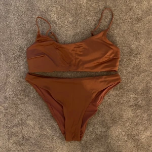 Brun bikini med sportig topp - Snygg brun bikini med sportig topp och smala axelband. Bikinin har en enkel och stilren design med högt skurna trosor. Materialet är mjukt och stretchigt, perfekt för strandhäng eller pool. Färgen är varm brun och modellen är klassisk utan extra detaljer.