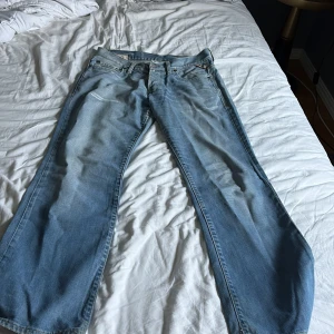 Ljusblå bootcut jeans från Jack Jones  - Säljer ett par ljusblå 90-tals jeans från Jack Jones med klassisk femficksdesign och bootcut-ben. Jeansen har snygga slitningar och kontrastsömmar, samt broderade detaljer på bakfickorna. Perfekta för en avslappnad och trendig look.
