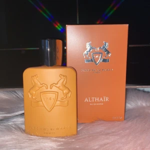 Parfums de Marly Althaïr  - Exklusiv parfym från Parfums de Marly, Althaïr Eau de Parfum. Flaskan är matt orange med upphöjt emblem och svarta detaljer. Kommer i matchande orange kartong med silverdetaljer. Lyxig och modern design, perfekt för dig som gillar unika dofter.