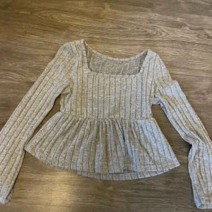 Grå ribbad blus med volang - Grå tröja ganska mjukt material, vet inte vart den är köpt men inte använd mycket alls, sitter bra. Den är nog xss,xs,s. Köpare står för frakt men pris kan gå ner lite 