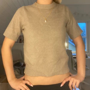 Beige stickad kortärmad tröja - Superfin beige stickad tröja med korta ärmar och ribbade kanter vid hals, ärmslut och nederkant. Enkel och stilren modell som är lätt att matcha med allt. Perfekt för dig som gillar en clean och chill look.