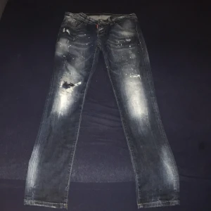 Dsquared2 slim jeans med slitningar - Snygga Dsquared2 jeans i mörkblå tvätt med slitningar, färgstänk och coola detaljer. Slim fit-modell med klassisk femficksdesign och orange kontrastsömmar. Perfekta för dig som gillar streetstyle och vill sticka ut lite extra.