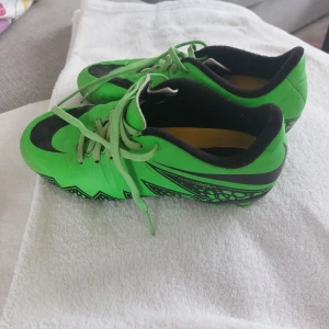 Nike Hypervenom gröna fotbollsskor - Säljer ett par Nike Hypervenom fotbollsskor i en riktigt grön färg med svarta detaljer och snörning. Skorna har mönstrad sula med dobbar för bra grepp på planen och är tillverkade i syntetmaterial. Perfekta för dig som vill sticka ut på fotbollsplanen.