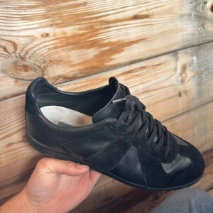Svarta Maison Margiela  Gats🐈‍⬛ - Säljer ett par riktigt feta Maison Margiela Gats i storlek 42 (passar 43). Skorna är i bra skick, dem har blivit lite creasade samt att dem har en blekt fläck på ena skosnöret. Går att vända skosnöret åt andra håller för att de ej ska synas eller köpa nya för en liten slant. Har digitalt kvitto på skorna! Tveka ej på att höra av dig vid funderingar, inga frågor är dumma frågor! Tack!🙌🏼🤩