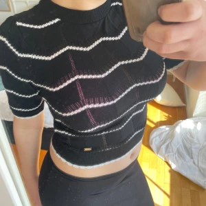 Svart stickad topp från Holly & Whyte - Säljer en svart stickad topp från Holly & Whyte by Lindex med vita horisontella ränder. Toppen är croppad och har korta ärmar samt ribbad halsringning och nederkant. Perfekt för dig som gillar en trendig och bekväm stil.