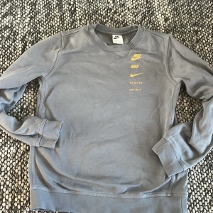 Grå sweatshirt från Nike - Säljer en grå sweatshirt från Nike och text på bröstet samt stor Nike-logga på ryggen. Tröjan har rund hals och långa ärmar. Perfekt för en sportig och avslappnad stil.