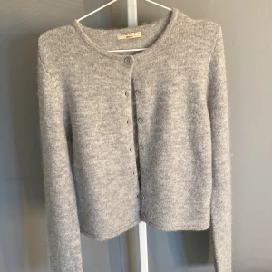 Ljusgrå kofta från Gina Tricot - Mysig ljusgrå kofta från Gina Tricot med rund halsringning och knappar framtill.