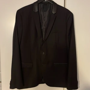 Svart kavaj från Kiomi med skinnkrage - Säljer en svart kavaj från Kiomi i storlek S. Kavajen har snygga detaljer med skinn på kragen och ficklock, två knappar framtill och klassisk passform. Perfekt för dig som vill ha en fräsch kavaj till studenten.