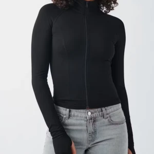 Svart tight jacka med dragkedja - Säljer en svart, figurnära jacka med hög krage och hel dragkedja framtill. Jackan har långa ärmar och en minimalistisk design som passar perfekt till jeans eller träningsbyxor.