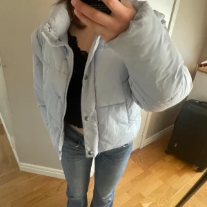 Ljusblå pufferjacka från Gina Tricot storlek S - Säljer denna härliga pufferjacka från Gina Tricot. Jackan har dragkedja och tryckknappar framtill, hög krage och långa ärmar. Den är varm, vacker och stilren. Har bara använt den ett fåtal gånger, så jackan är i nästintill nyskick🩵