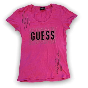 Guess t-shirt - Rosa Guess tröja med coolt svart + silvrigt tryck och rhinestones! nån enstaka rhinestone har ramlat av men skulle inte säga att det syns alls. Passar XS-S har klippt bort tvättlappen då den skavde men den ska tvättas i 30 grader, helst ut och in för att bevara tryck så länge som möjligt. Den har inga fläckar eller hål 