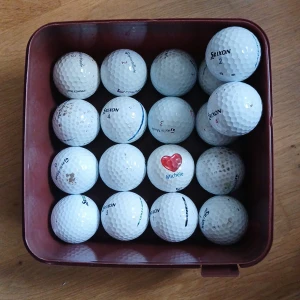 Golfbollar i  - Säljer en samling vita golfbollar i en rödbrun plastlåda. En av bollarna har ett rött hjärta och texten 'Michele' på sig. Flera olika märken syns på bollarna, bland annat Srixon. Perfekt för golfentusiasten!