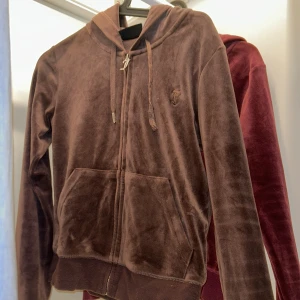 Brun velour hoodie från Juicy Couture - Mjuk och skön brun hoodie i velour från Juicy Couture. Jackan har dragkedja framtill, huva med snören och två stora fickor. Perfekt för en avslappnad och trendig look. Ena metallbiten har lossnat och därav Priset
