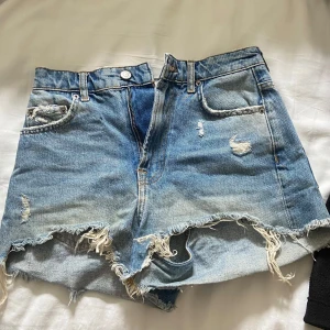 Blå jeansshorts från Zara - Säljer ett par blå jeansshorts från Zara med fransiga kanter och slitna detaljer. Shortsen har hög midja, fickor fram och bak samt dragkedja och knapp. Perfekta inför sommaren!! Säljer massa billiga plagg då jag rensar garderoben så kolla gärna in de! Alla kläder går att diskutera priset på!!