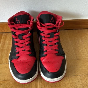 Air Jordan Mid Svart röda  - Svart röda Jordan 1 skor knappt använda men har creesats på framsidan som ni ser på bilden. Skorna är i ett bra skick. Hör gärna av er vid frågor 