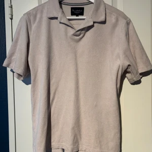 Beige pikétröja från Brodelei - Säljer en stilren beige pikétröja från Brodelei i storlek M. Tröjan har korta ärmar, klassisk krage och är tillverkad i ett mjukt frottématerial. Perfekt för en avslappnad men snygg look.