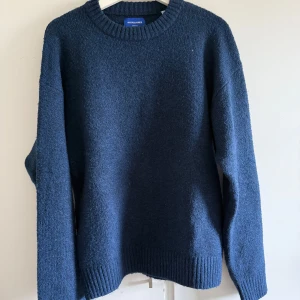 Mörkblå stickad tröja från Jack & Jones - Säljer en mörkblå stickad tröja från Jack & Jones. Tröjan har rund halsringning, ribbade muddar vid ärmslut och nederkant samt en klassisk, enkel design. Perfekt för kyligare dagar och lätt att matcha med olika outfits. Storlek M. Den är lite nopprig men annars bra skick