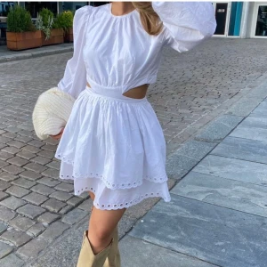 Vit klänning med öppen rygg och volang - Superfin vit kortklänning med långa puffärmar, öppen rygg och utskärning i midjan. Klänningen har dubbla volanglager i kjolen och broderade kanter. Superfin till studenten eller sommaren!!🥰🥰