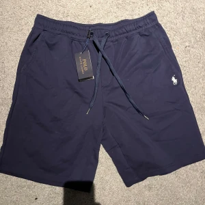 Polo Ralph Lauren shorts - Snygga marinblå shorts från Polo Ralph Lauren med klassisk logga broderad på ena benet. Shortsen har snörning i midjan och en bakficka. Perfekta för sommardagar för ett bra pris, kom dm vid frågor