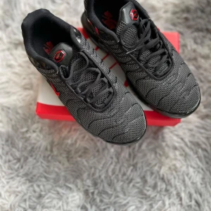 Svarta Nike sneakers med röda detaljer - Säljer ett par svarta Nike sneakers med snygga röda detaljer och mönstrad ovandel. Skorna har svart snörning, rund tå och platt sula med röd accent undertill. Perfekta för dig som gillar sportig stil och vill ha något bekvämt till vardags.