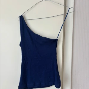 Mörkblå one shoulder topp  - Säljer en mörkblå one shoulder topp från Cubus. Toppen är ribbad och har en smal axelrem på ena sidan och är axelbandslös på andra. Jag bär vanligtvis storlek S/M. Tvek inte på att höra av dig vid frågor eller prisförslag!