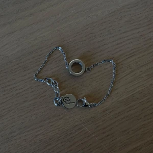 Silverfärgat armband med cirkeldetalj. Edblad  - Säljer ett stilrent armband i silverfärg från Edblad. Armbandet har en tunn kedja och en rund cirkeldetalj i mitten samt en liten bricka med Edblads logga vid låset. Perfekt för dig som gillar minimalistiska smycken.