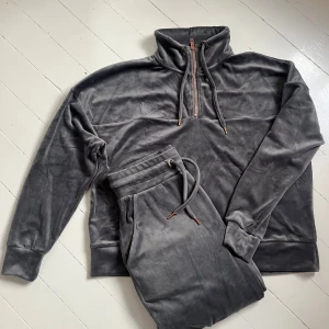 Mörkgrått mjukisset i velour - Mjukt och skönt mörkgrått mjukisset i velour med tröja och byxor. Tröjan har hög krage och halv dragkedja framtill. Tröjan har även långa ärmar och snörning i halsen. Byxorna har resår och snöre i midjan. Perfekt för en avslappnad och trendig look. Är knappt använda, så nästan nya. Skriv för fler bilder💞