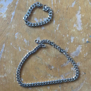 Silverfärgat armband och halsband i kedjemodell - Säljer ett set med ett armband och ett halsband i silverfärgad metall. Halsband 40,5 cm armband 17 cm. Båda har en klassisk kedjelänk-design med robust känsla och blanka ytor. Perfekt för dig som gillar stilrena accessoarer med lite edge.