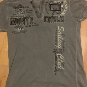  Violento - Grå/grön t-shirt från Violento med flera tryck på framsidan, bland annat texten 'Monte Carlo' och 'Sailing Club'. T-shirten har korta ärmar och knappar vid halsen för en snygg detalj. Perfekt för en avslappnad stil.