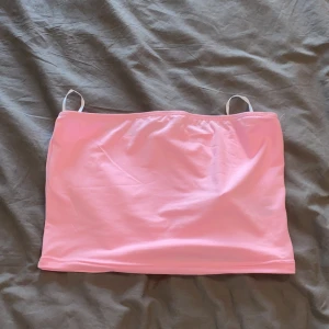 Ljusrosa tubtopp - Säljer en ljusrosa tubtopp med smala axelband. Enkel och stilren design, perfekt för varma dagar eller som layering-plagg. Mjuk och stretchig för en bekväm passform. Storlek XXS