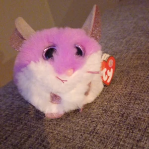 Söt rund bok om mus från Ty - En gullig, rund bok i form av en mus från Ty. Boken är lila och vit med stora glittriga öron, svans och rosa detaljer. Perfekt för dig som gillar söta och mjuka samlarböcker. Cirka 10 cm hög.