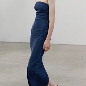 Mörkblå axelbandslös jeansklänning - Säljer en mörkblå, axelbandslös långklänning i jeansmaterial. Klänningen har en tight passform och passar mig som har S i vanliga fall