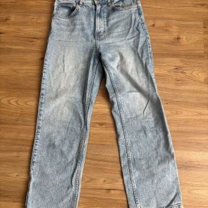 Ljusblå raka jeans från Never Denim - Säljer ett par ljusblå jeans från Never Denim med raka ben och klassisk femficksdesign. Jeansen har hög midja, knappgylf och diskreta slitningar för en vintagekänsla. Perfekta till vardags och lätta att matcha med olika stilar.