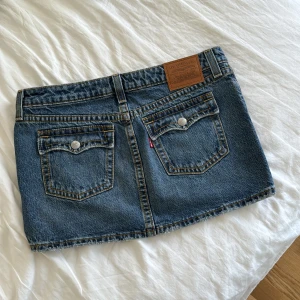 Jeanskjol från Levi's - Säljer en blå jeanskjol från Levi's med fickor både bak och fram. Kjolen har synliga nitar. Kjolen är kort och har en rak passform. Perfekt för sommaren! Det är storlek XS, passar bra på mig som bär XS/S 🩷Orginalpris: 719 kr