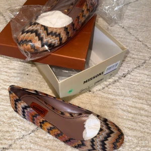 Mönstrade ballerinaskor från Missoni - Säljer ett par ballerinaskor från Missoni med ikoniskt zickzackmönster i svart, brunt, orange och beige. Skorna har rund tå och platt sula, och är tillverkade i textil med läderdetaljer invändigt. Perfekta för dig som gillar färg och mönster!