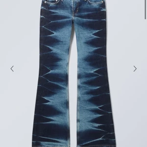 Blå bootcut jeans med mönster - Säljer ett par blå bootcut jeans med unikt batikmönster längs benen. Klassisk femficksmodell med dragkedja och knapp framtill. Perfekta för dig som vill sticka ut med din stil!