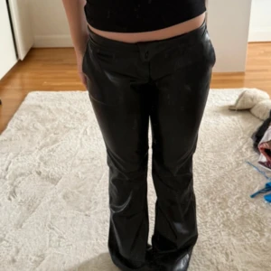Svarta bootcutbyxor - Snygga svarta byxor i skinnimitation med bootcut-modell. Byxorna har en mittemellan midja och klassisk stängning framtill. Perfekta för att lyfta vilken outfit som helst med en edgy vibe. Dom är helt nya utan prislapp och inte använda. Lite stora i storleken men jätte bekväma!!