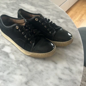 Svarta Lanvins med vit sula - Säljer ett par svarta Lanvins med snörning och med glans. Skorna har ovandel i mocka, samt vita sulor med svarta detaljer. Perfekta för en stilren och avslappnad look. Har några vita repor men dem syns inte på långt hål dessutom lite smutsigt sula på undersidan som går att tvätta och insidan är ganska använt. Mockan är helt okej och har tappat lite sin mjukhet på en liten del av den vänstra skon. Annars är den i helt okej skick och är i storlek 8 (43) Går bra att hämtas 