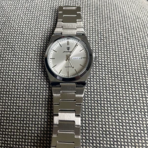 Silverfärgad klocka  - Snygg silverfärgad klocka med kvartsurverk. Den har en stilren vit urtavla med dag- och datumvisning. Armbandet är i rostfritt stål och ger en elegant look. Perfekt för den som gillar en klassisk stil.