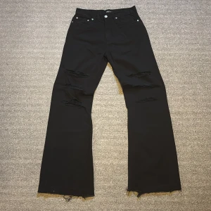 Custom flared bootcut jeans - Säljer ett par svarta jeans med distressing på knäna. Byxorna har avklippta kanter nertill.  42 cm midja, 120 cm längd 